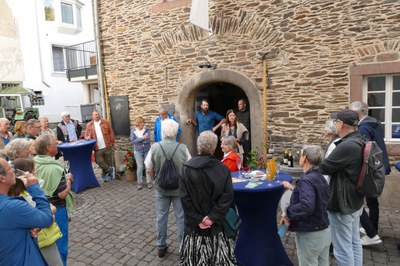 Begrüßung der Pat*innen im Hof des Weinguts Böcking Gruppe von Gästen mit Sektgläsern vor dem historischen Bruchsteingebäude des Weinguts, vorne Stehtische