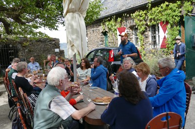 Bei Wein und Flammkuchen gab es Einblicke in die Arbeit im Steilhang Gäste an einer langen Holztafel im Freien, ein Mann im Stehen erzählt mit Weinglas in der Hand.