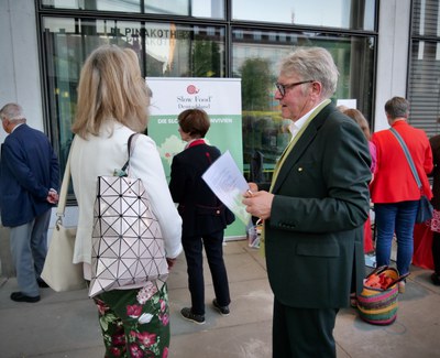 Ein Mann mit Unterlagen spricht mit einer Frau, dahinter ein Roll-up von Slow Food Deutschland zu den Convivien vor der Glasfassade