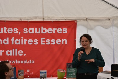 Tag der Fische 2026, Katharina Benecke Vortrag (c) Slow Food Deutschland Frau spricht mit Mikrofon vor rotem Slow-Food-Banner im Zelt