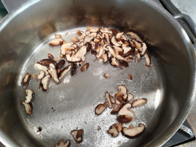 Pilze werden kräftig angeschwitzt Geschnittene Shiitake-Pilze werden in einem Edelstahltopf in Öl angebraten