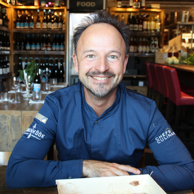 Thomas Sampl, Chef-Alliance-Koch aus Hamburg, lächelt in die Kamera, im Hintergrund Weinregale der Hobenköök