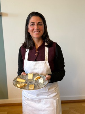 Sechs Käse, sechs Geschichten (c) Yasemin Çelik Yasemin Çelik in weißer Schürze hält lächelnd einen Teller mit sechs verschiedenen Käsesorten